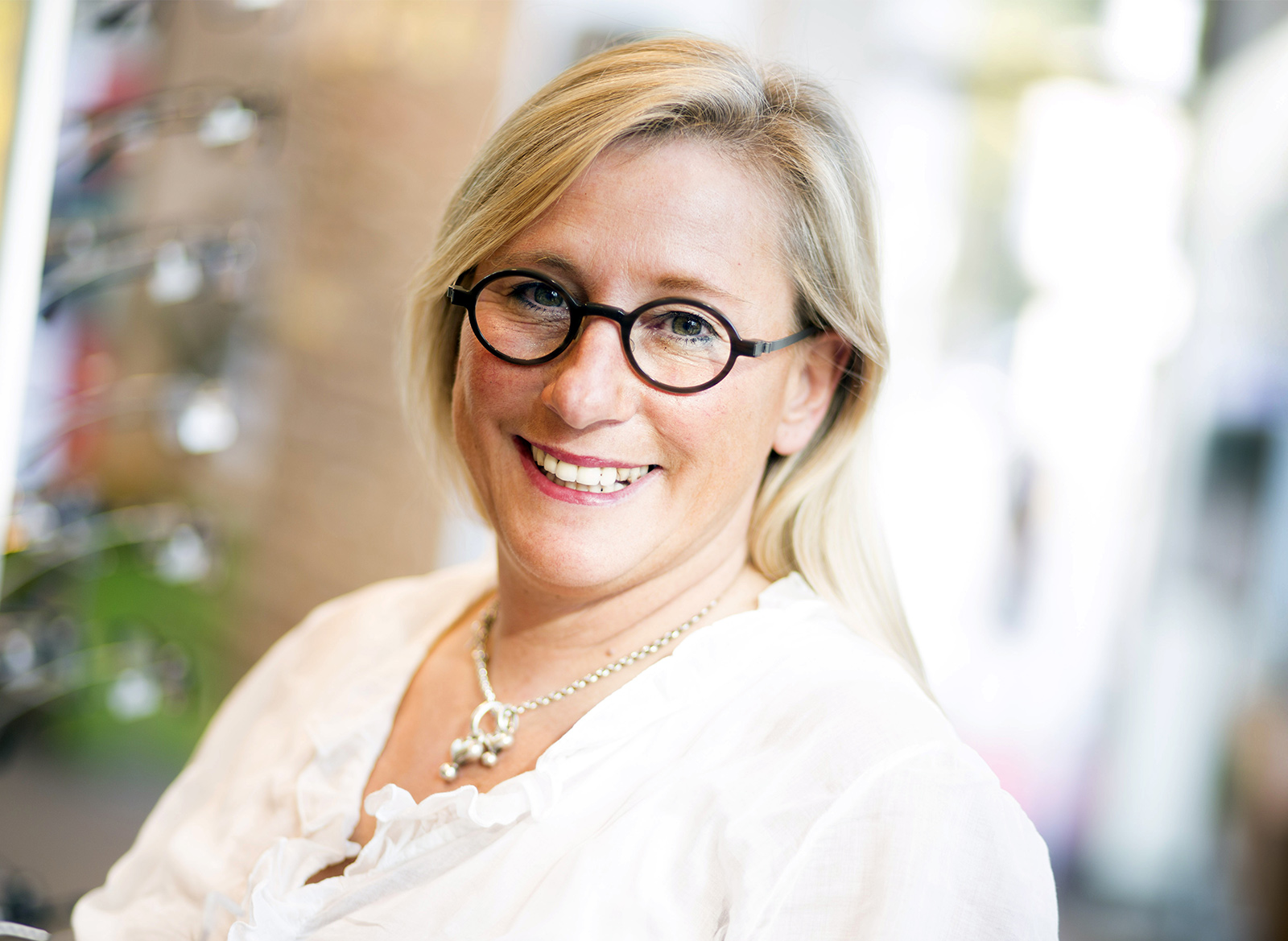 J. Brecht, Augenoptikermeisterin bei Kunk neue optik in Bremen Lächelnde Frau mit Brille mit weißen Oberteil.